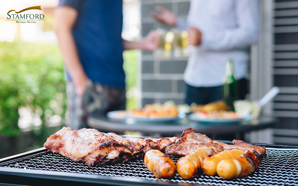 People enjoying drinks near a BBQ grill.